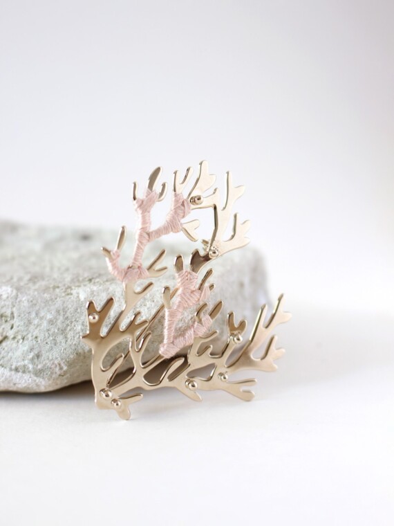 Broche corail sable rosé Maldives. Elle est présentée devant une pierre naturelle.