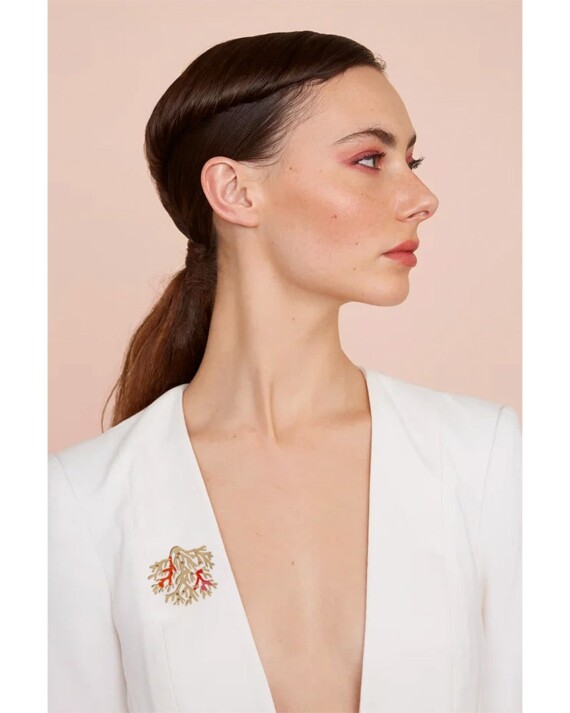 femme poortant sur ses habits la broche corail grenadine maldives. Une broche dorée et brodée de fil rouge.