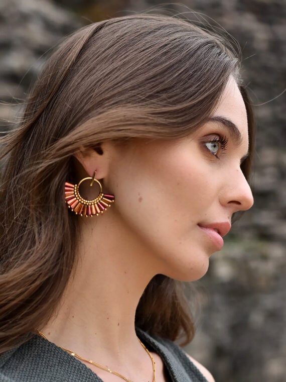 Boucles d'oreilles colorées et élégantes et forme d'éventail, portées par une femme. Nommées : Quetzal magenta